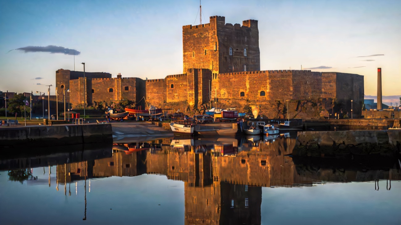 Carrickfergus Castle glowing gold at sunset, reflected in the still harbour water