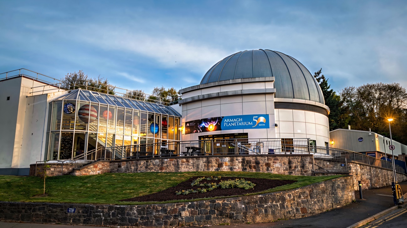 The silver dome and glass atrium of Armagh Planetarium against a blue evening sky