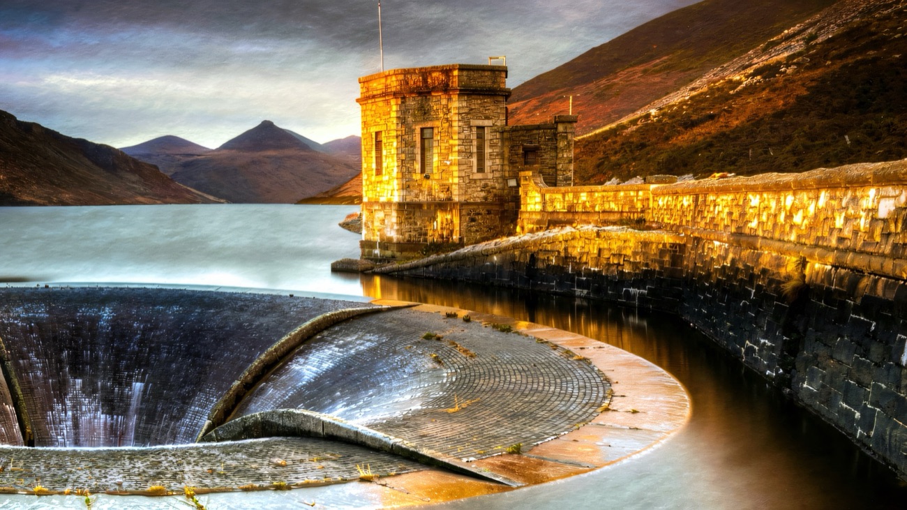 The great stone dam and tower at Silent Valley glowing in evening light, with the Mourne peaks behind the reservoir
