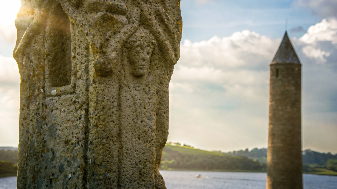 A carved face on the old high cross, the round tower rising beyond