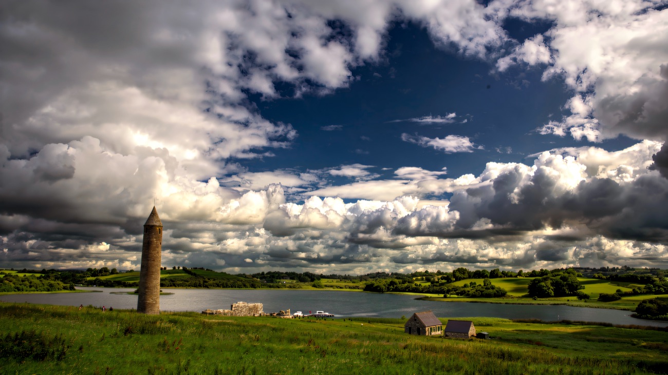 The tower and church on their green island under a vast cloud-filled sky