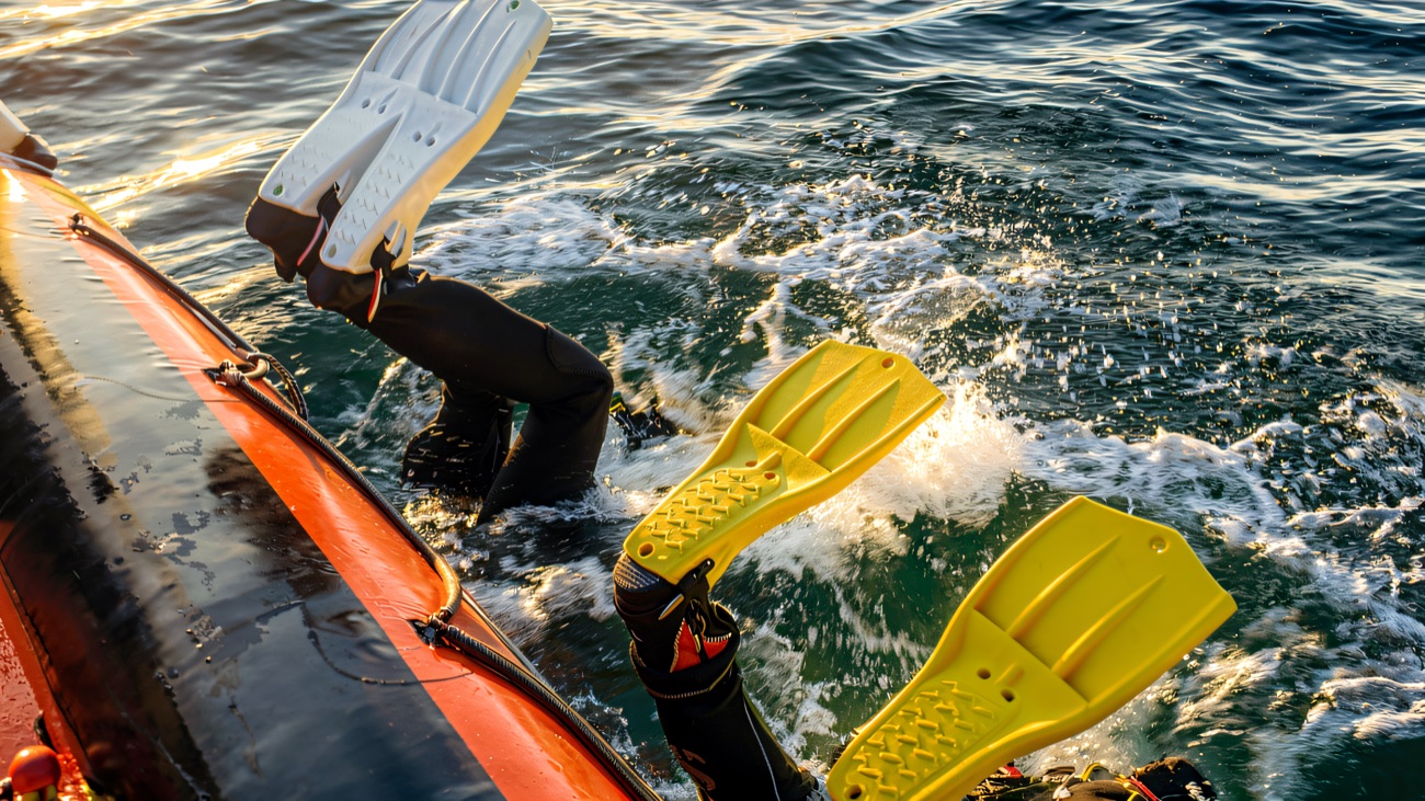 Divers rolling backwards off the side of an orange RIB into the sea