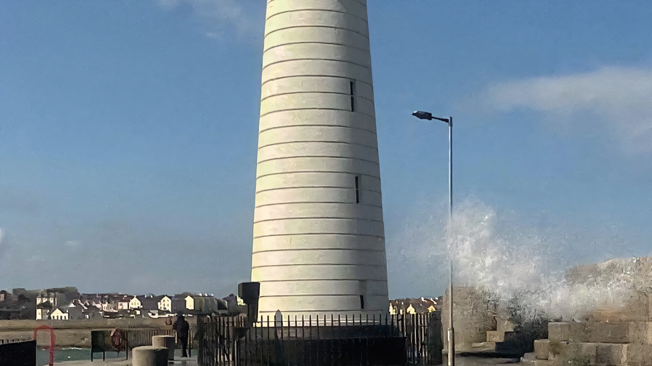 Waves burst over the pier beside the lighthouse on a breezy afternoon.