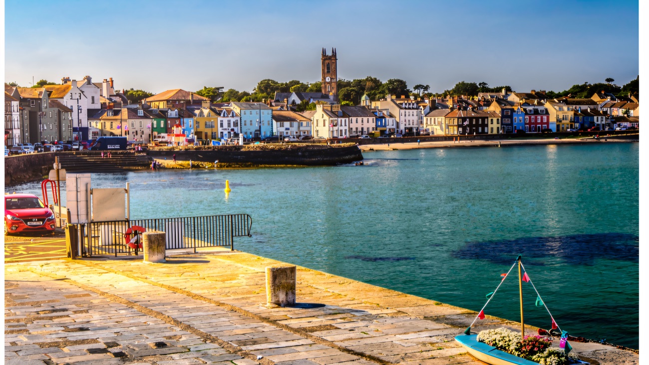 Looking back from the pier to Donaghadee's painted seafront houses and church tower, with a flower-filled boat on the quay