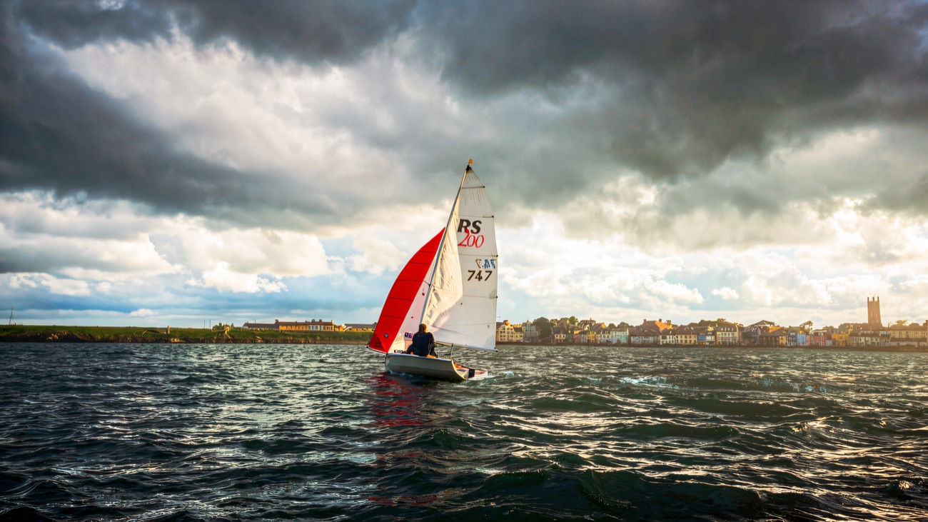 A lone dinghy with a red spinnaker skimming past the colourful seafront