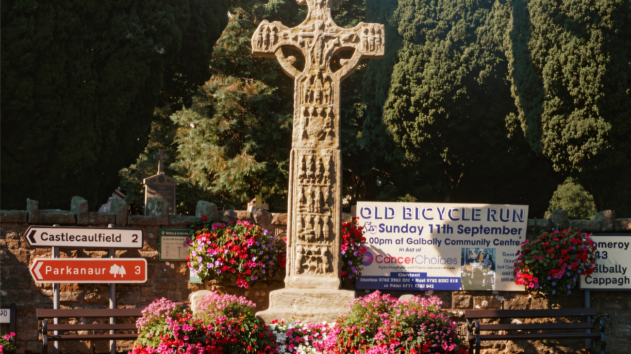 The high cross at the heart of the village, ringed with summer flowers.
