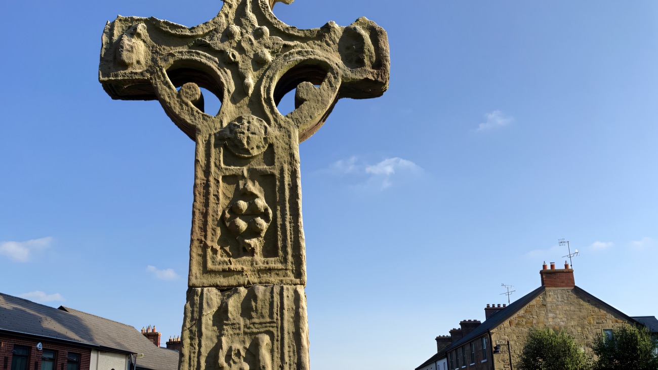 The ancient high cross rising against a clear blue sky, its ring and shaft carved with scenes from scripture.