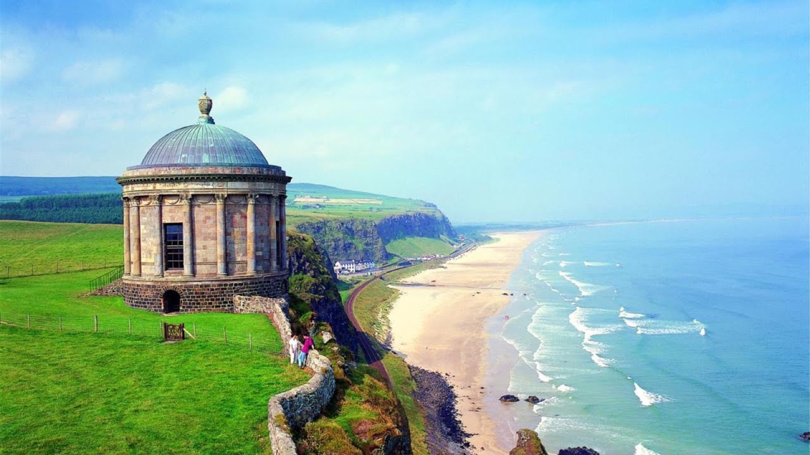 Mussenden Temple perched on the clifftop above Downhill Beach, with the long strand sweeping away to the horizon under a bright blue sky