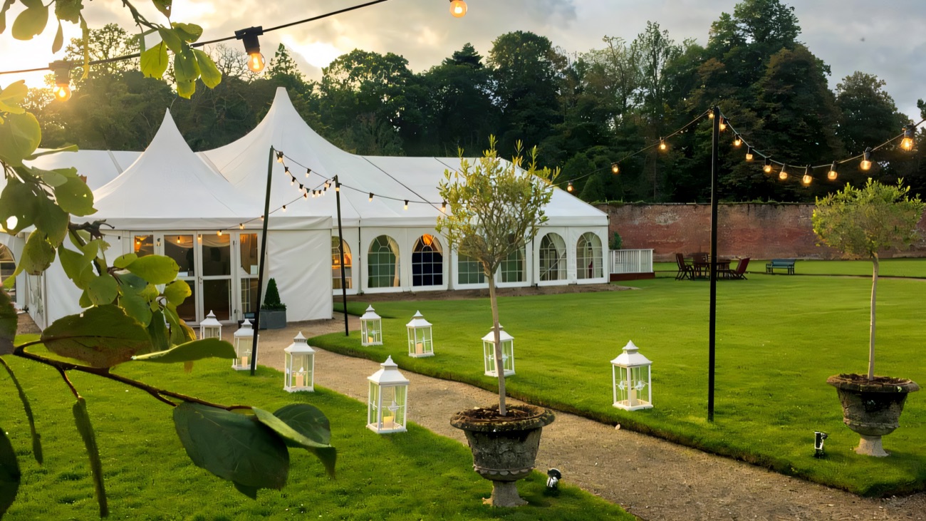 A white events marquee in the walled garden strung with festoon lights and lanterns