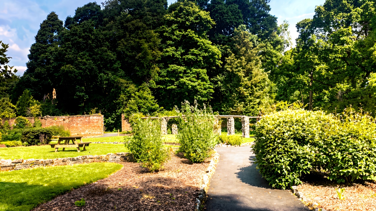 The walled garden at Drum Manor with a gravel path, planted beds, a picnic table and old brick walls with arched gateways