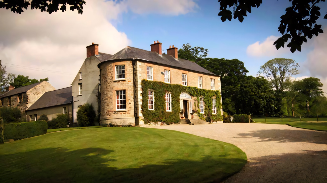 The ivy-clad Georgian facade of Drumcovitt House with its bow tower and brick chimneys, a broad green lawn and gravel sweep in front