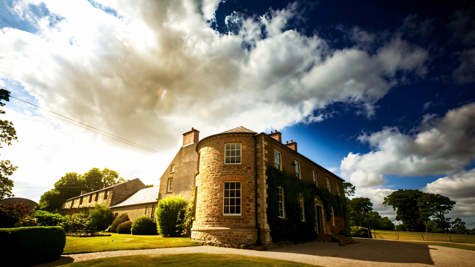 The stone Georgian front of Drumcovitt House with its rounded bow-fronted tower, sash windows and ivy, above a curving lawn and gravel drive
