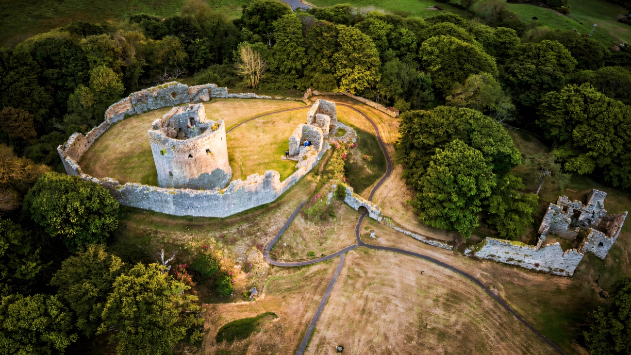 Aerial view of the whole Dundrum Castle ruin on its hilltop — round keep, curtain walls and grassy bailey