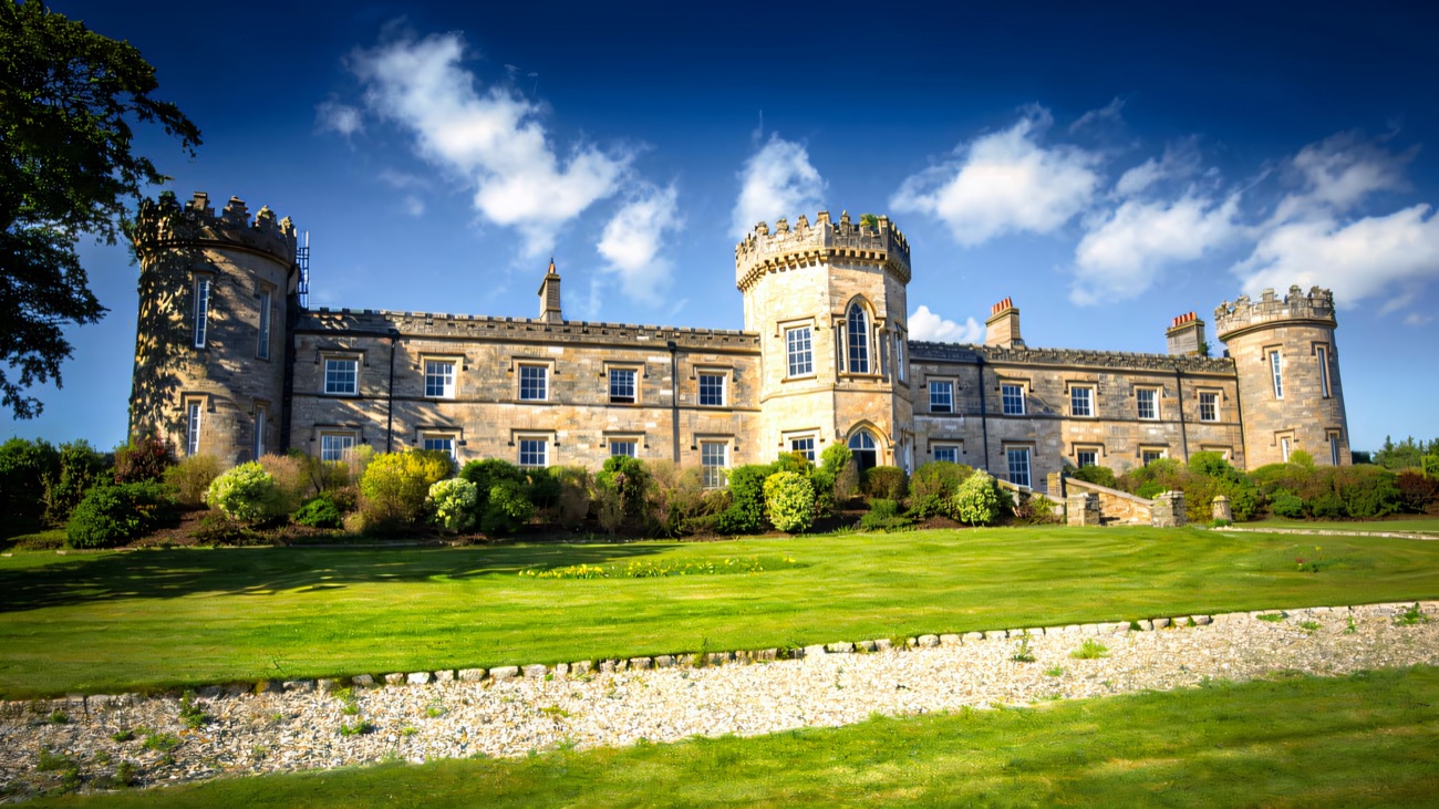 The full castellated front of Dungiven Castle with three round turrets under a bright blue sky