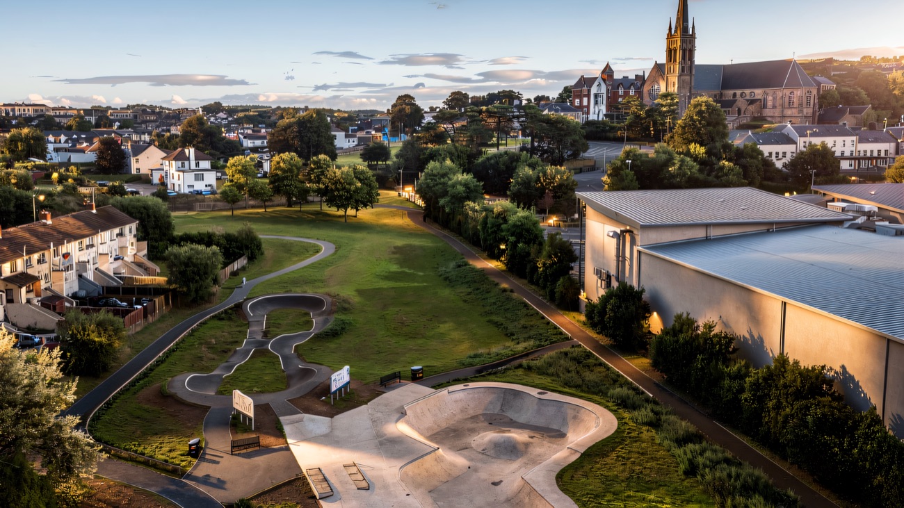 Aerial view of the concrete bowl and tarmac pump track, with Downpatrick's cathedral spire beyond