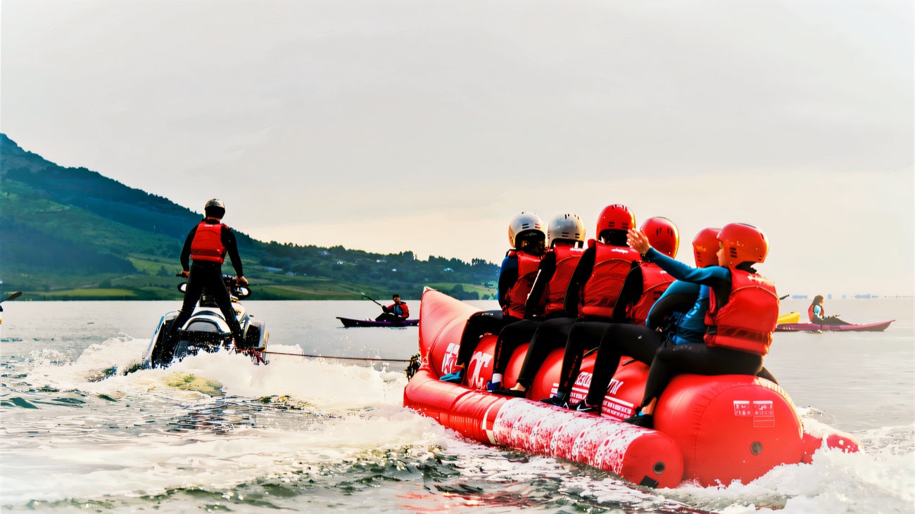 Helmeted riders hanging on to the banana boat behind a jet ski