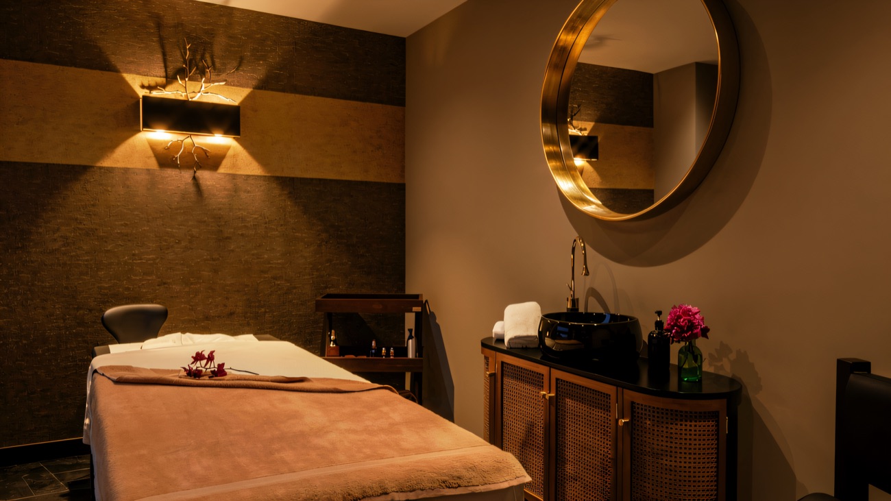 A quiet treatment room with a heated bed, warm lighting and a round gold mirror.