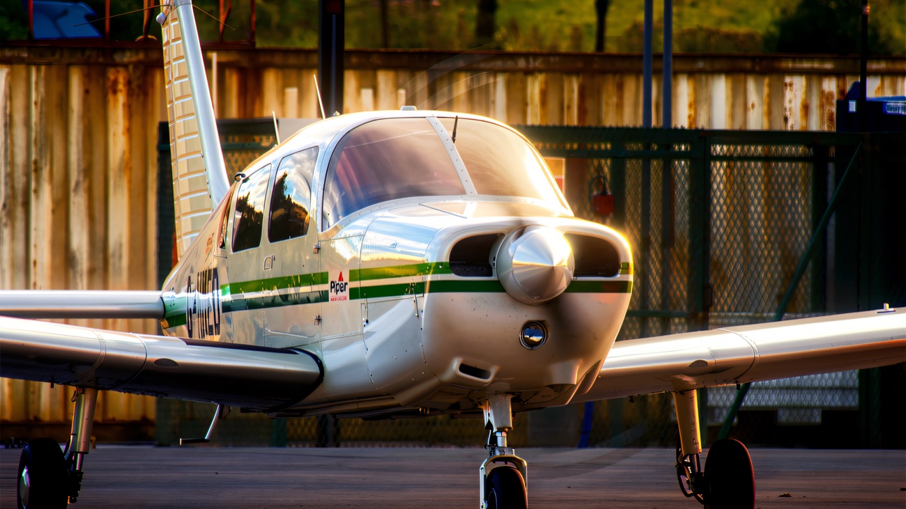 A white and green light aircraft parked on the apron, seen head-on with its propeller and nose wheel