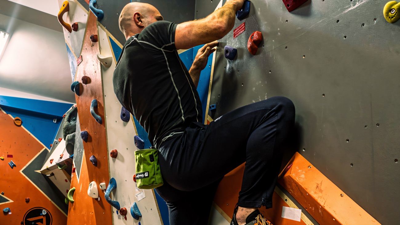 A climber reaching for holds on the grey and orange bouldering wall