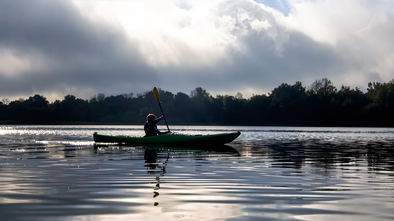 A lone paddler out on mirror-calm water under a soft, misty sky.