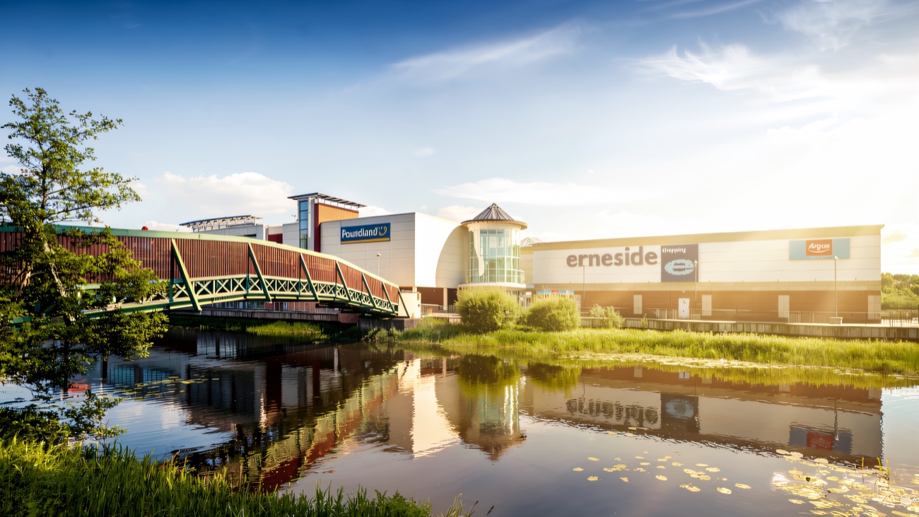 The green footbridge across the River Erne to Erneside, with the glass rotunda entrance and Poundland and Argos signs beyond