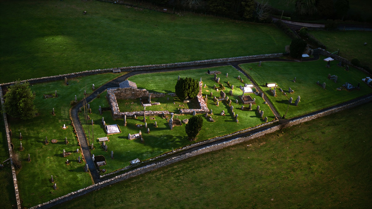 An aerial view of the walled graveyard with the ruined church at its centre and fields all around