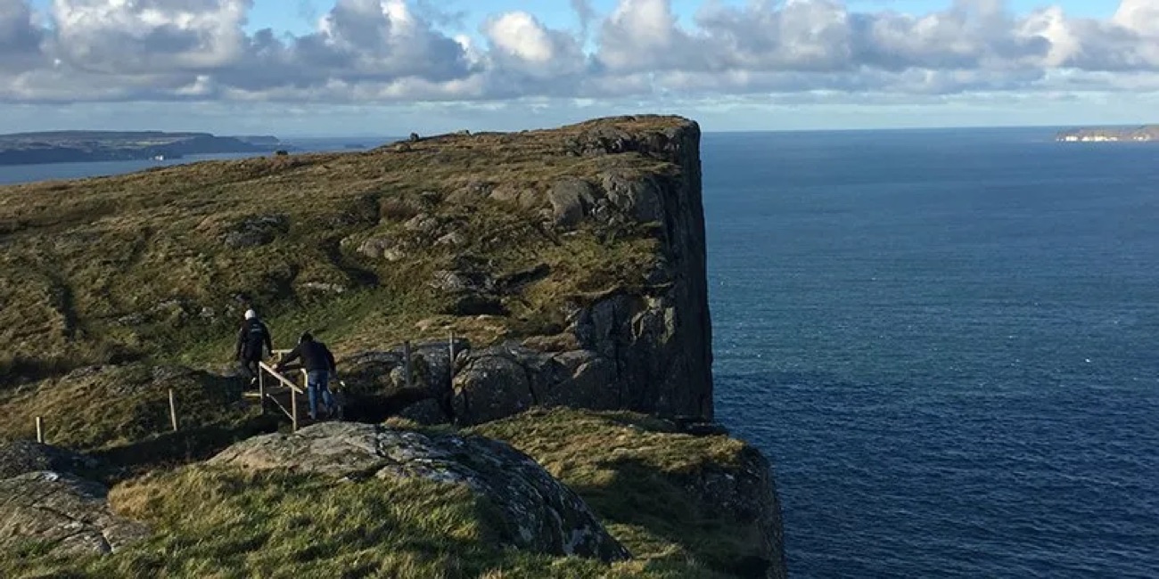 Two walkers at the sheer edge of Fair Head with the vast cliff dropping away to the sea