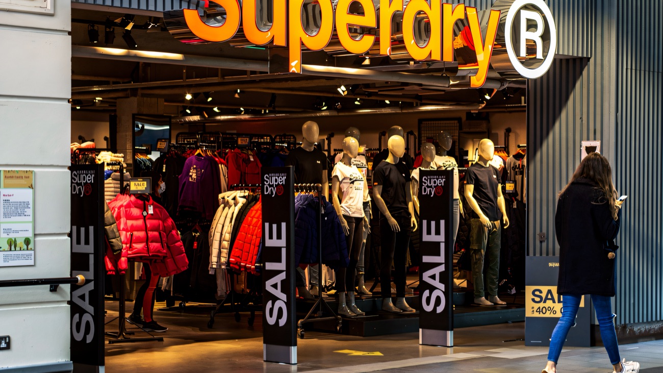 The Superdry storefront under Fairhill's exposed-brick mall frontage, a shopper walking past