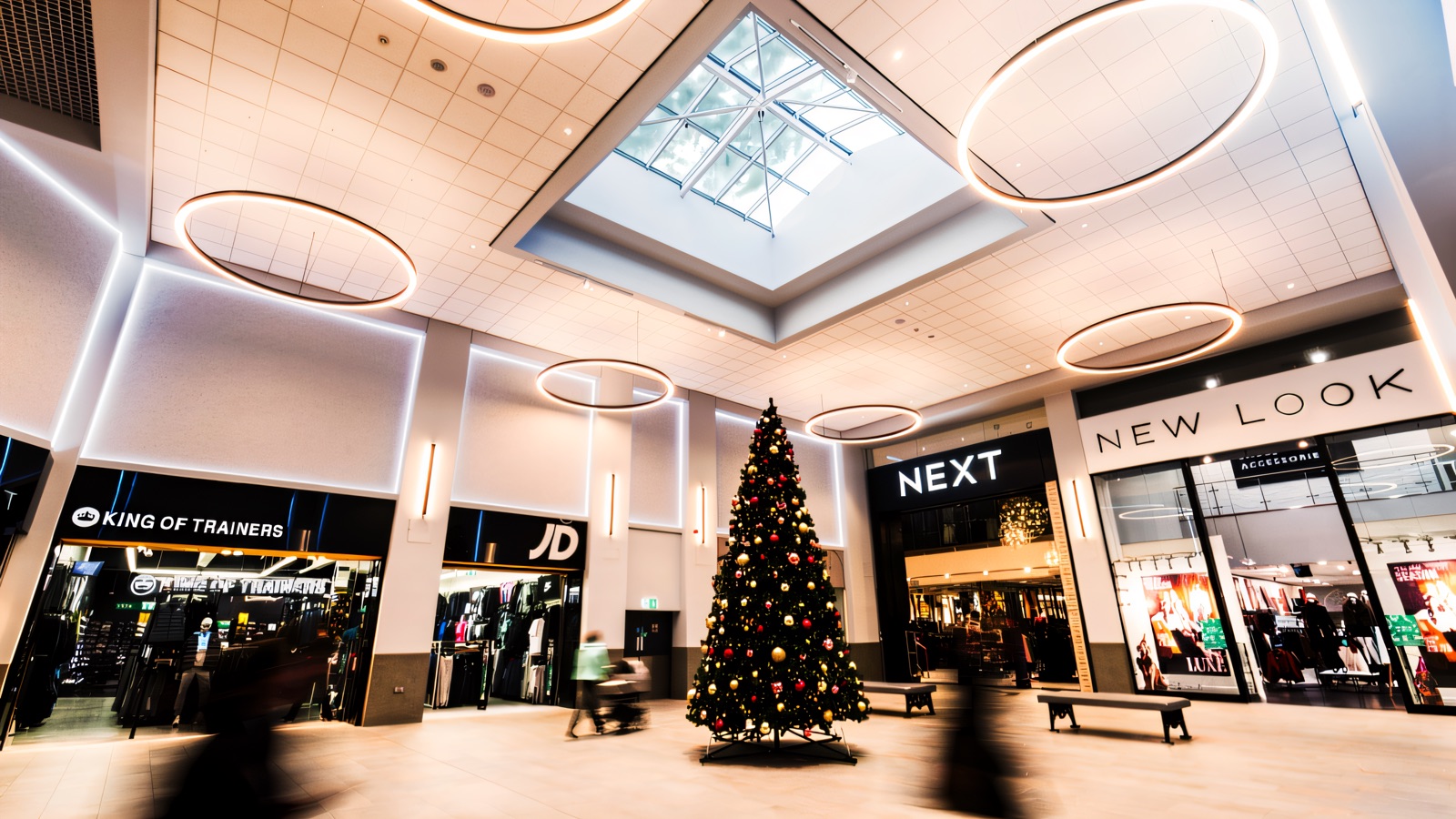 Inside the refurbished Fairhill mall — a bright skylight and ring-lit ceiling over the Next and New Look shopfronts, with a Christmas tree in the middle of the walkway