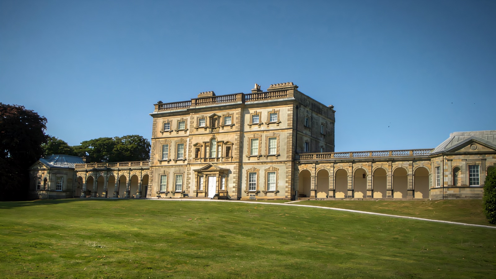 The grey Georgian house at Florence Court with its curved colonnade wings and a wide green lawn under a clear blue sky