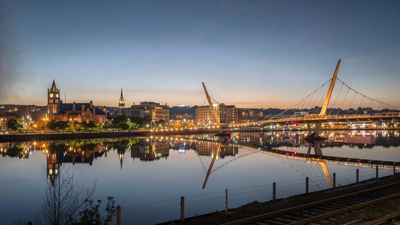 The Peace Bridge and Derry skyline mirrored in the Foyle at dusk.