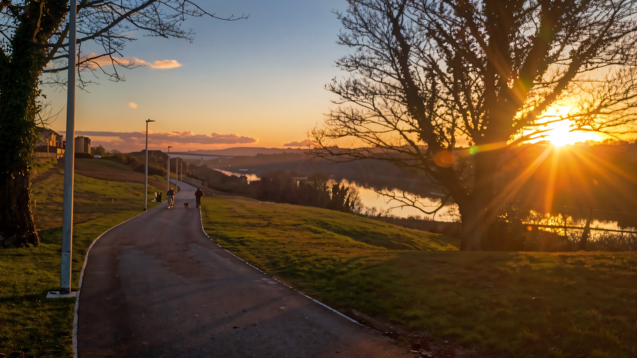 The riverside path glows in golden light beside the River Foyle