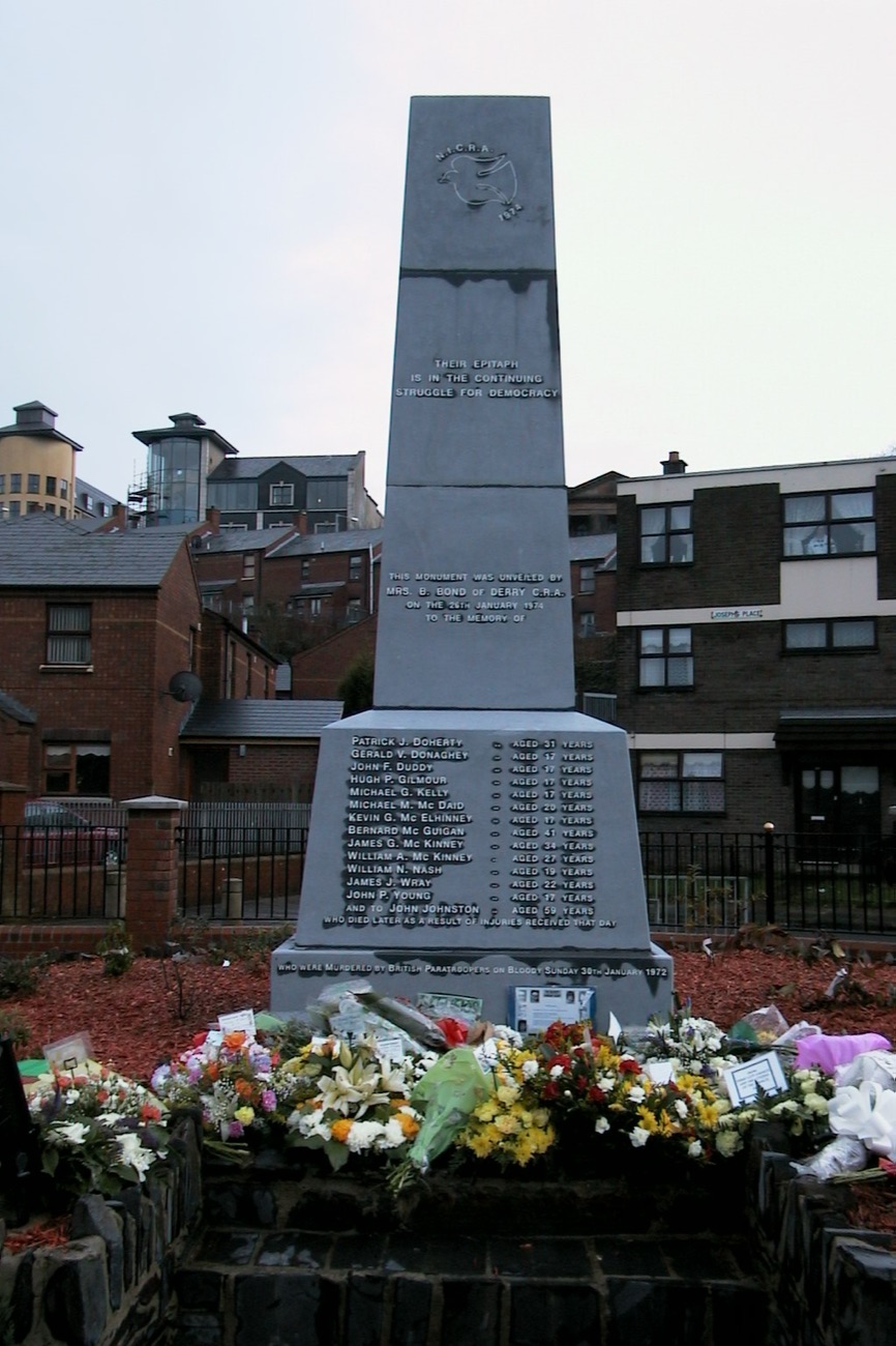 The Bloody Sunday Memorial, a tall stone obelisk with flowers laid at its base, in the Bogside