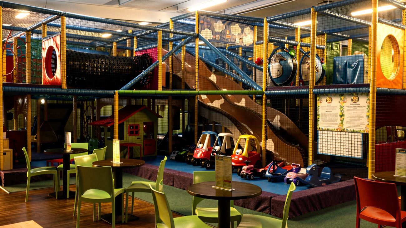 Big climbing frame, wavy slide and ride-on cars beside the cafe tables