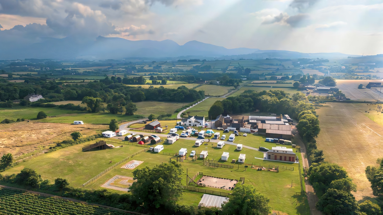 Aerial view of the Funny Farm Adventures site near Castlewellan, with a campsite field, farm buildings and the Mourne Mountains along the horizon