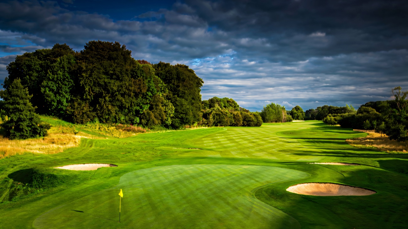 A manicured green with bunkers and flag on the Galgorm Castle golf course under a dramatic sky