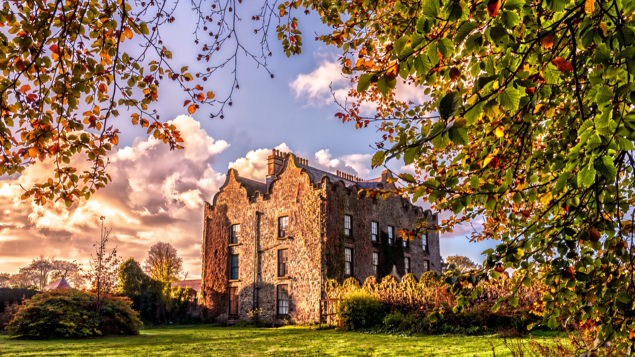 Galgorm Castle set in its lawns, framed by autumn trees at golden hour