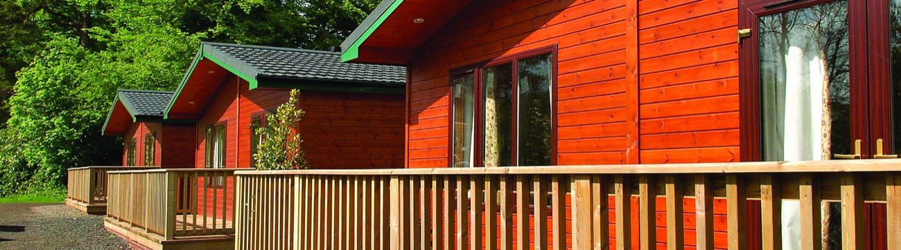 A row of timber-clad riverside log cabins with their own decking at Galgorm