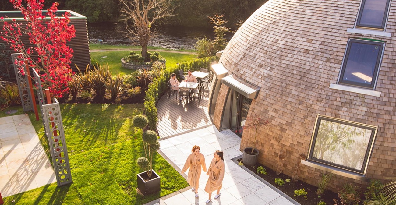 A domed shingle-clad spa building in the thermal village gardens at Galgorm, ringed by trees and lawns
