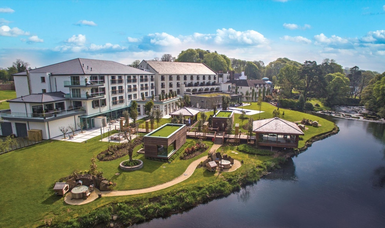 Aerial view of the riverside thermal spa village at Galgorm, its pods, cabanas and pools laid out along a bend of the River Maine