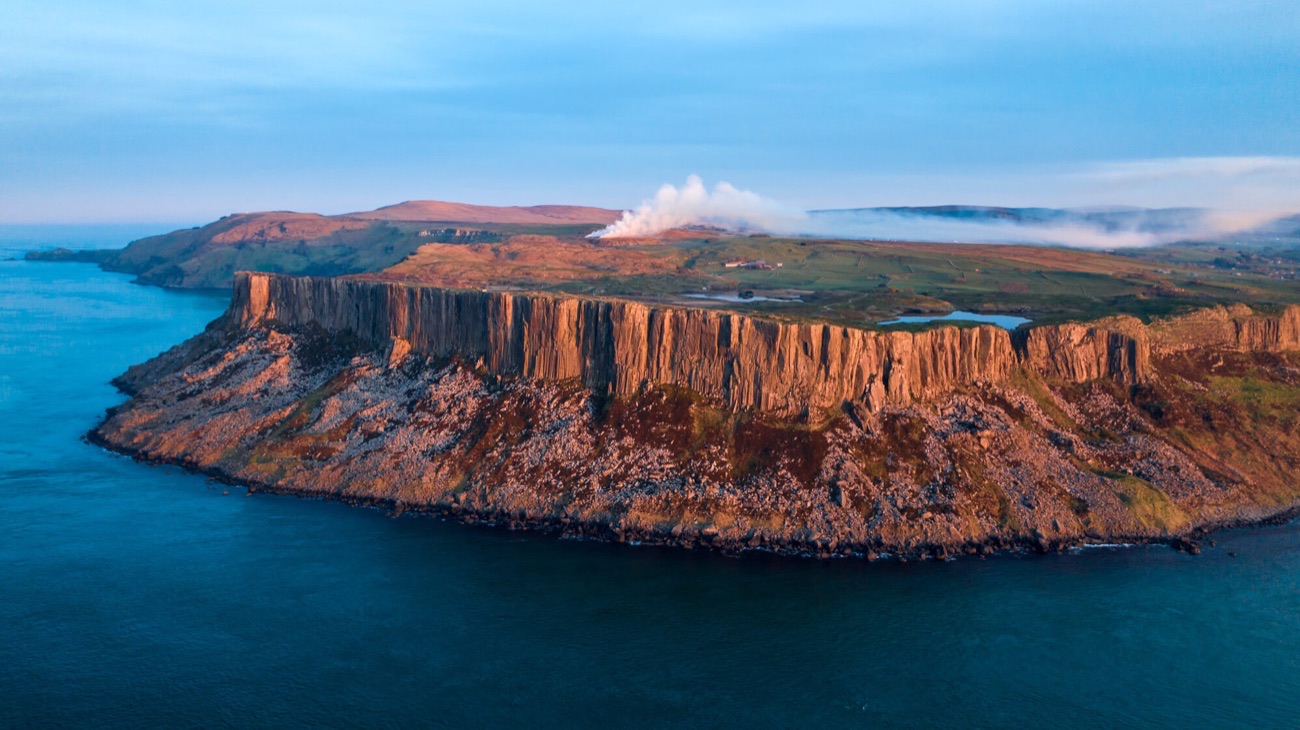 The great cliff face of Fair Head glowing at sunset above a deep blue sea