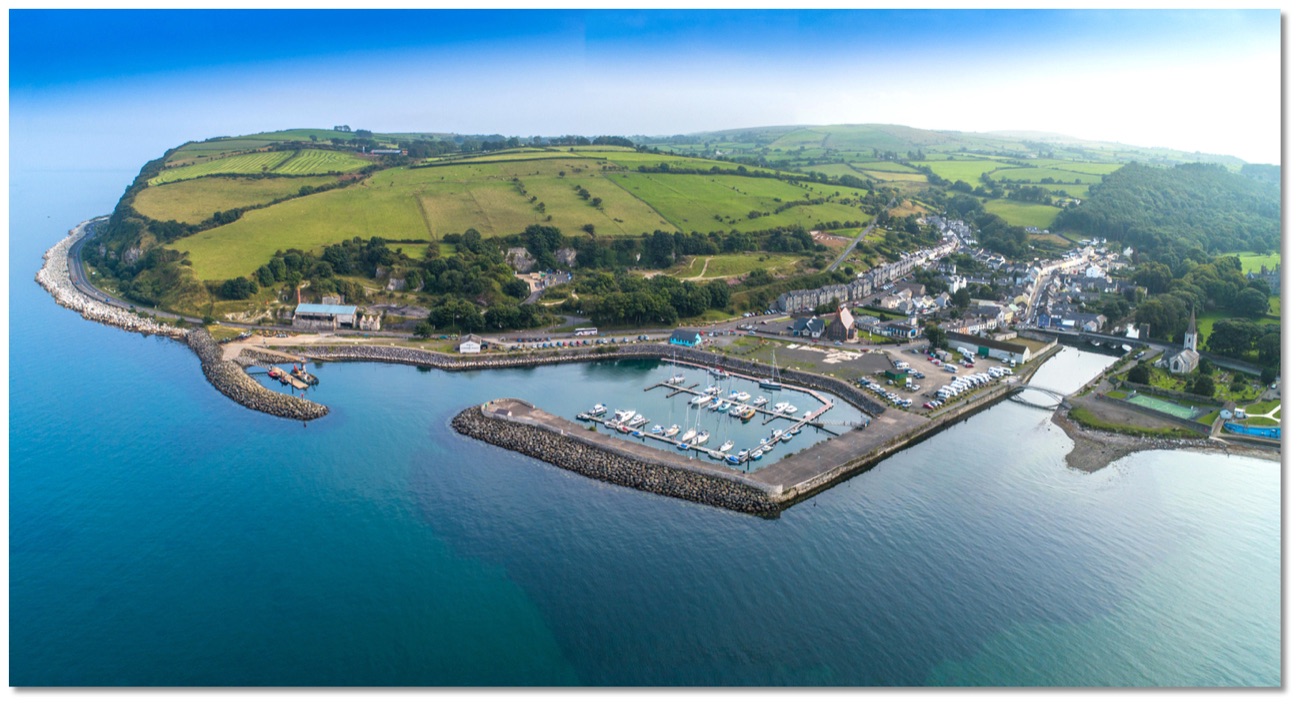 Wide aerial panorama of Glenarm village, its marina and the patchwork green fields of the Glens sweeping down to the sea