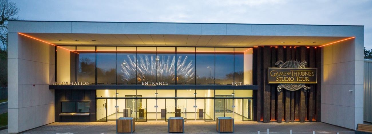 The Game of Thrones Studio Tour entrance building at dusk, glass frontage lit warm