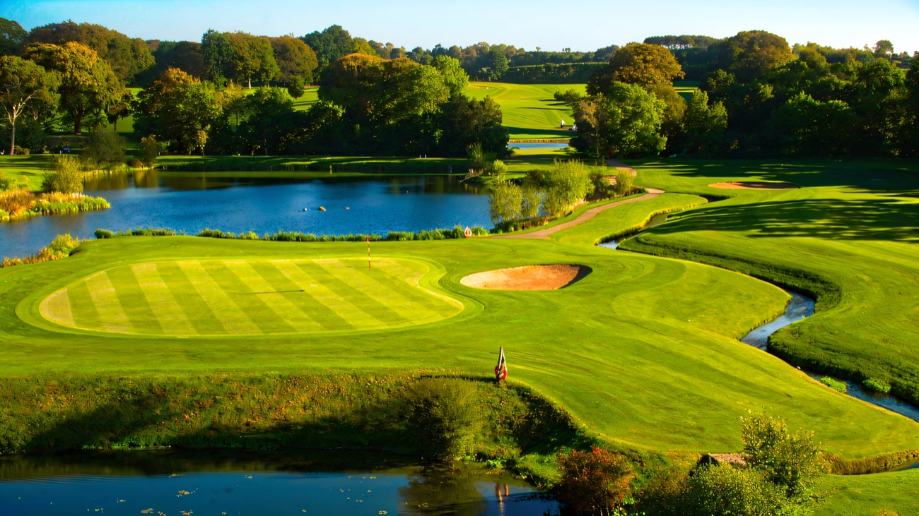 A manicured green and flag on Gracehill Golf Club, water and mature trees behind