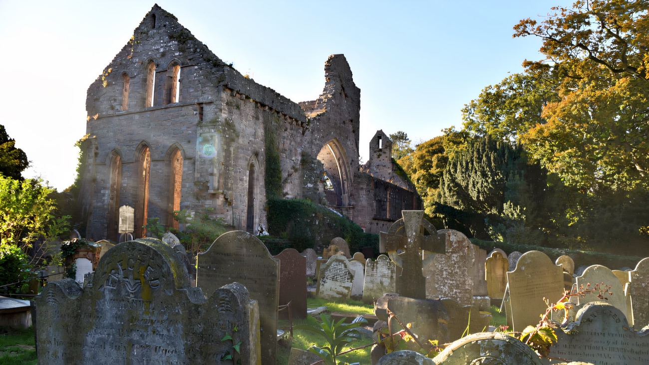 The abbey ruins rising behind the old graveyard, framed by autumn trees.