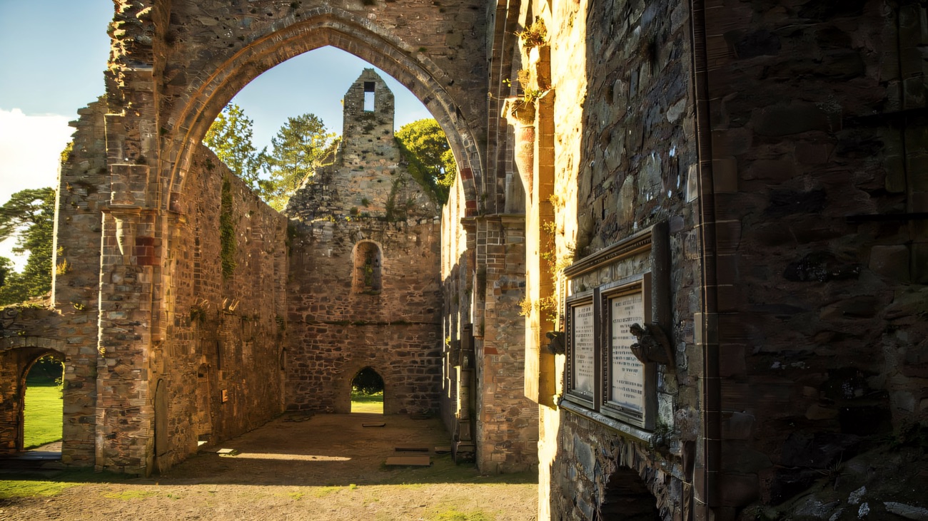 A pointed gothic arch opening into the roofless nave, sunlight raking across the stone.