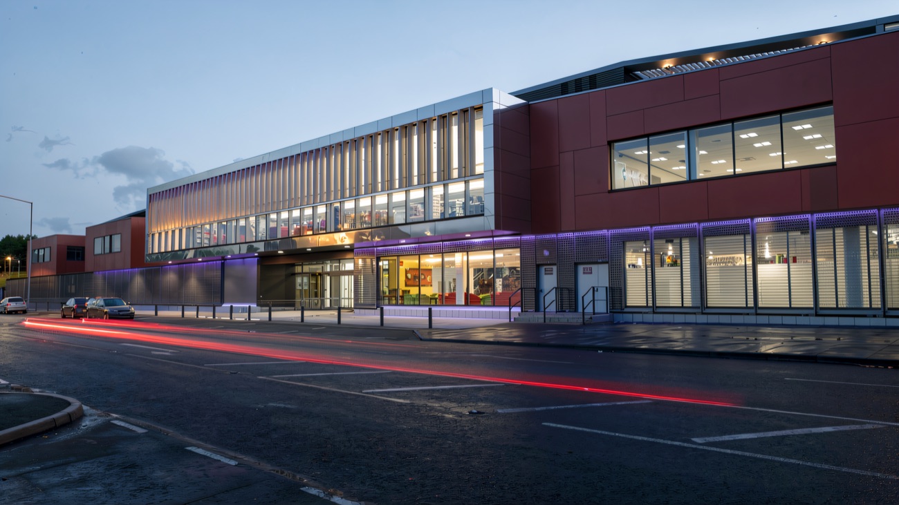 The centre's long glass-and-red frontage lit up at dusk