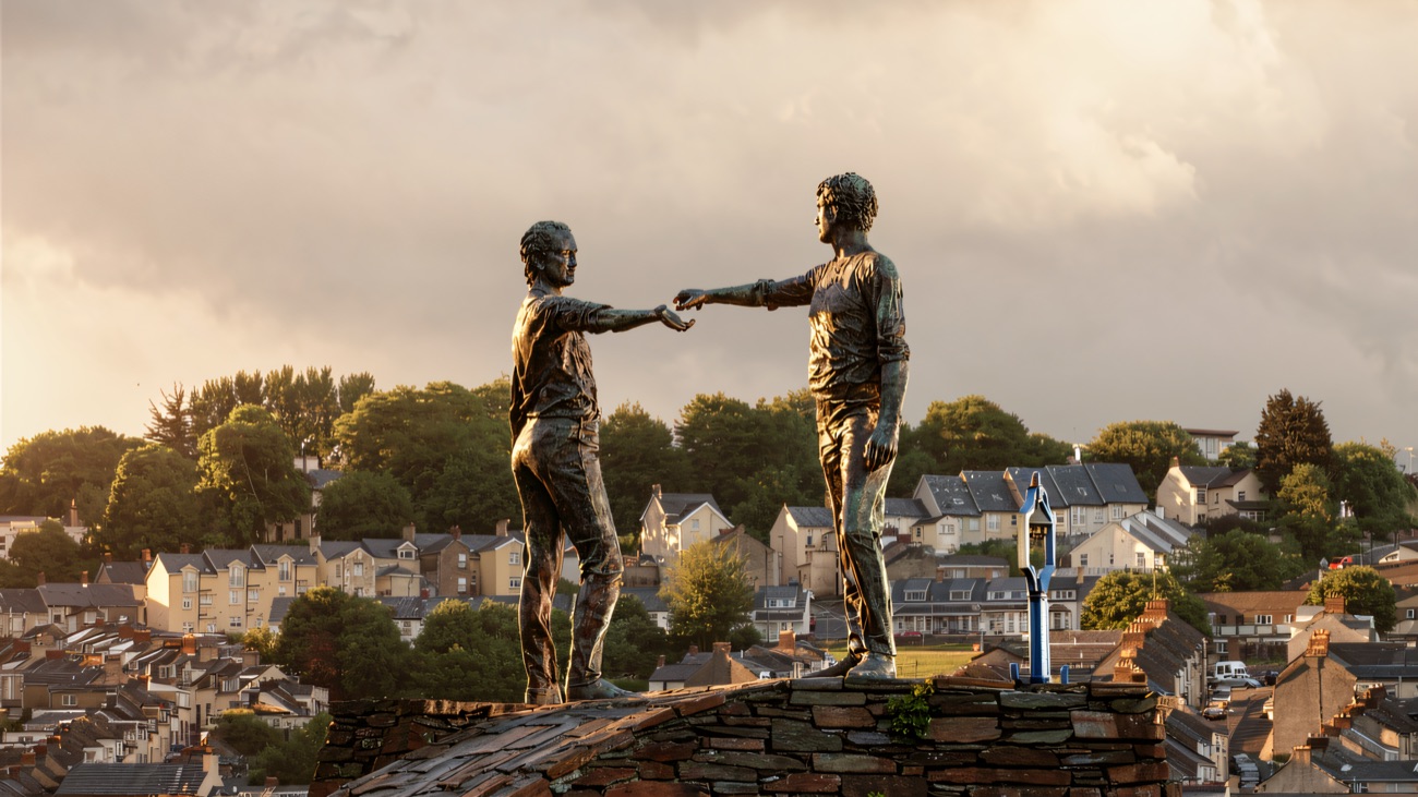 The bronze figures reaching toward each other above the rooftops of the city.