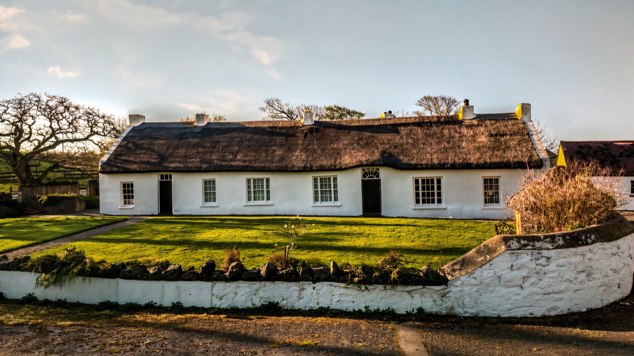 Hezlett House seen from the front on a sunny day, its dark thatched roof and white stub chimneys above a low whitewashed stone wall