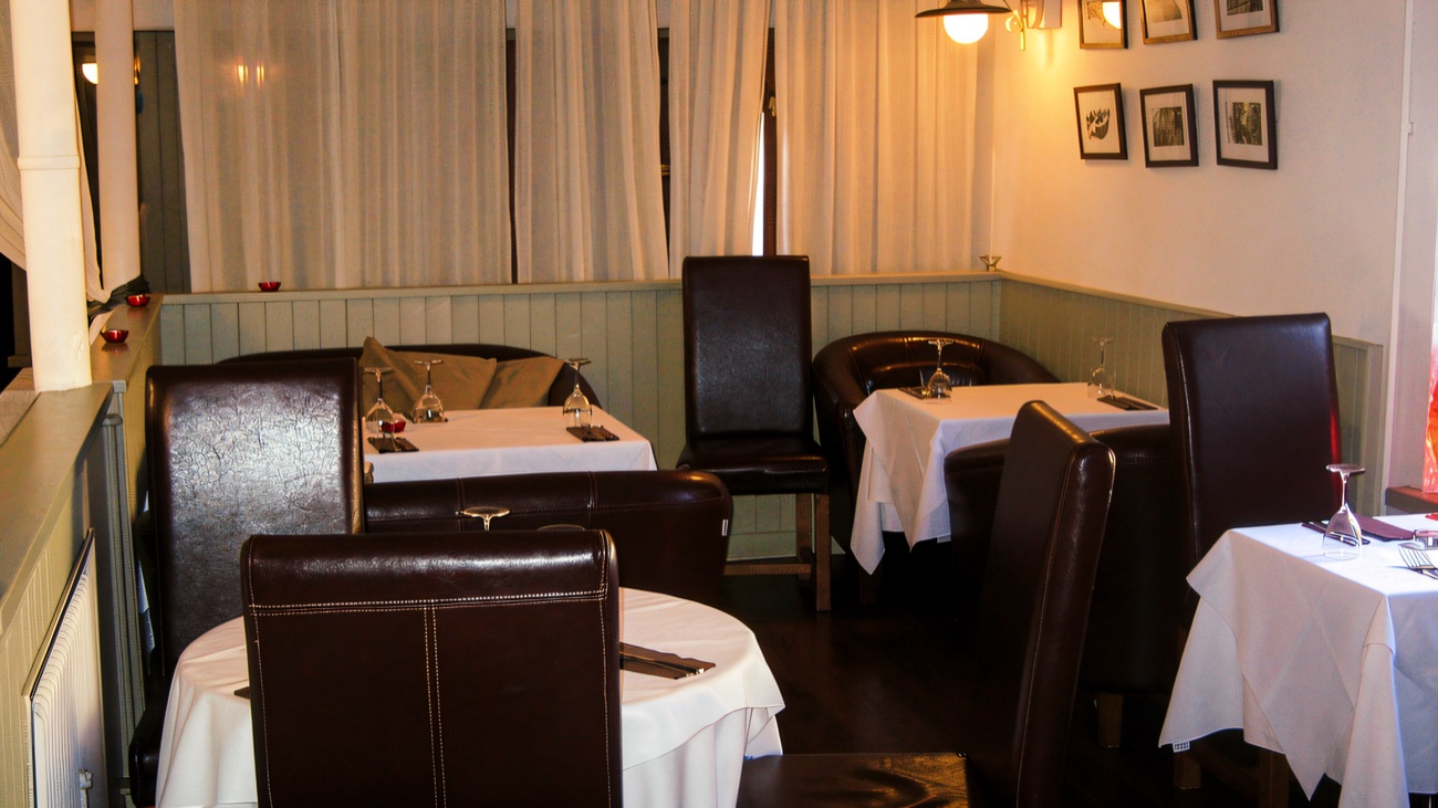A quiet dining room with white-clothed tables and framed pictures on the wall